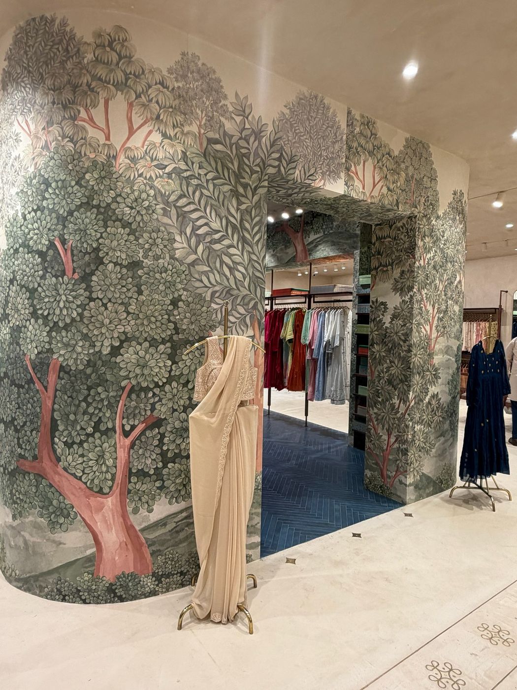A draped ivory saree displayed against the hand-painted tree mural